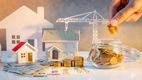 Real estate or property development. Construction business investment. Home mortgage loan rate. Hand putting coin in currency glass jar with Coin stack, banknotes, house and crane models on the table.